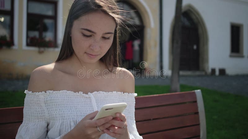 ładna kobieta pisze SMS w komórce siedzącej na zewnątrz