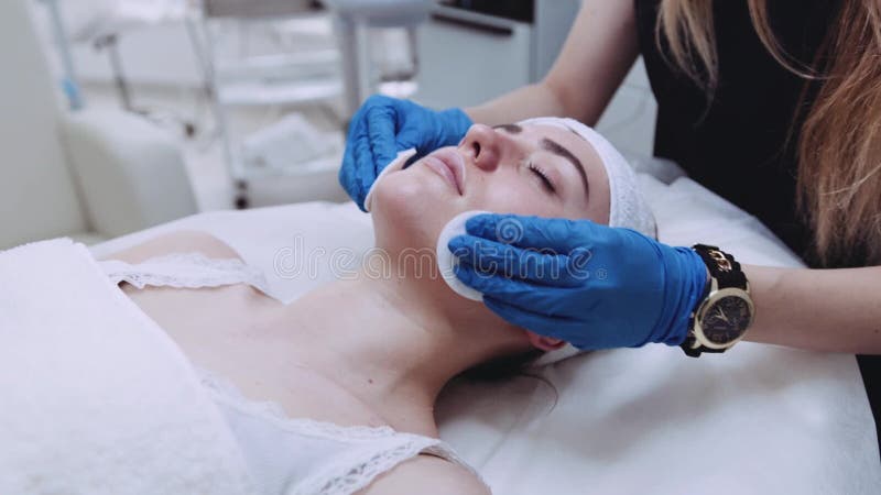 Ładna kobieta z zamkniętymi oczami, kłama na cosmetologistâ€™s stole dermatolog używa bawełniane gąbki