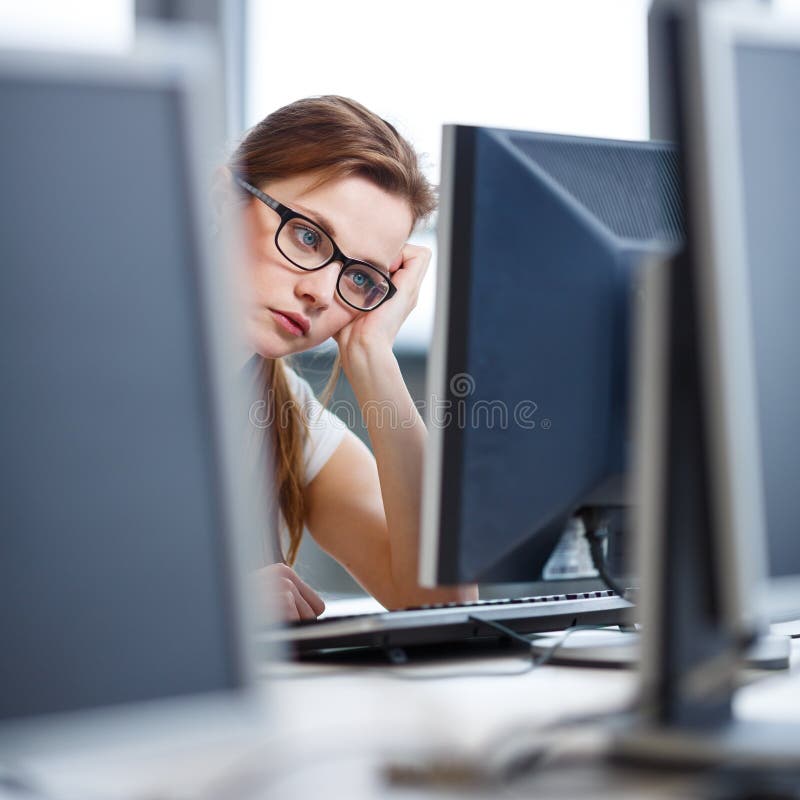 Pretty, female student looking at a desktop computer screen, learning unpleasant news about her exam results. University/office/school concept. Pretty, female student looking at a desktop computer screen, learning unpleasant news about her exam results. University/office/school concept