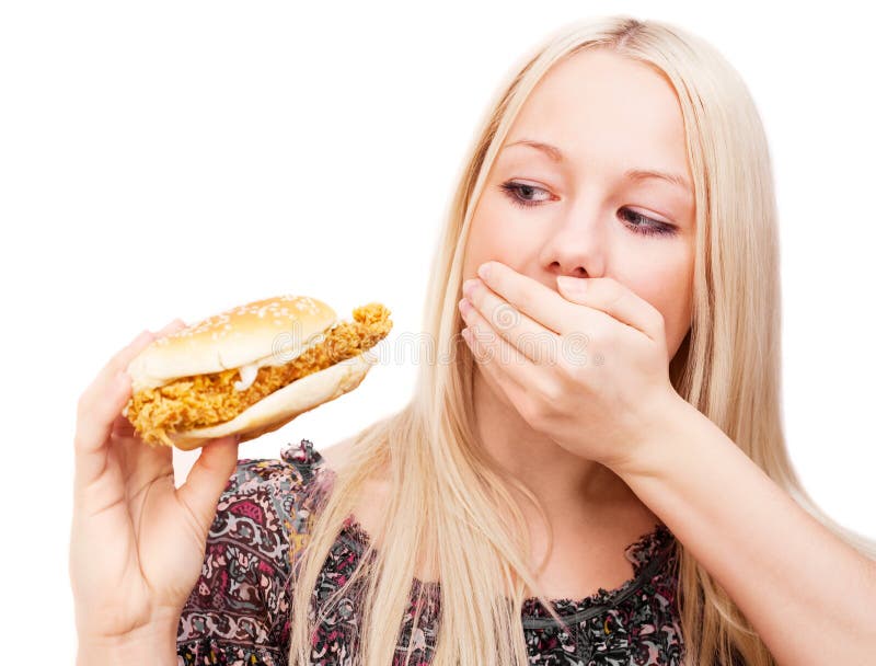 Young woman refusing to eat a hamburger with chicken and closing her mouth with a hand , isolated against white background. Young woman refusing to eat a hamburger with chicken and closing her mouth with a hand , isolated against white background