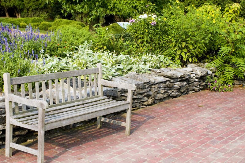 A wooden bench sits in front of a summer seasonal flower garden. A wooden bench sits in front of a summer seasonal flower garden.