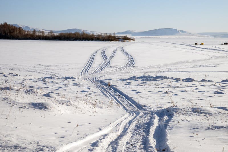 Ślad od snowmobile na śnieżnym jeziorze z rybakami w tle zdjęcia stock Ślad od snowmobile na śnieżnym jeziorze z rybakami w tle zdjęcia stock