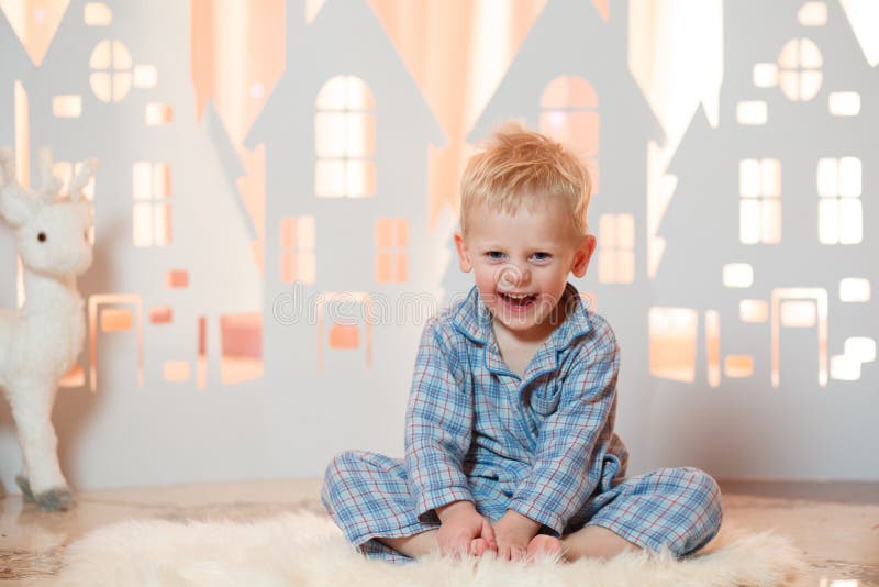 Śliczna blondynka włosy chłopiec w sleepwear blisko boże narodzenie zabawki papieru domów obrazy stock Śliczna blondynka włosy chłopiec w sleepwear blisko boże narodzenie zabawki papieru domów obrazy stock