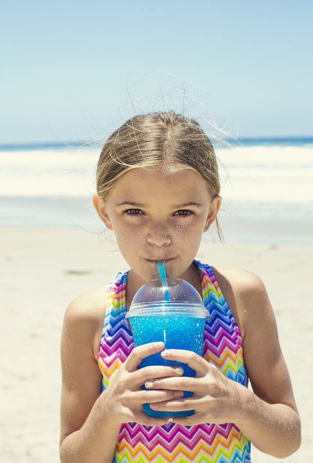 Śliczna dziewczyna pije błękitnego lodowego napój przy plażą podczas wakacje zdjęcie stock Śliczna dziewczyna pije błękitnego lodowego napój przy plażą podczas wakacje zdjęcie stock