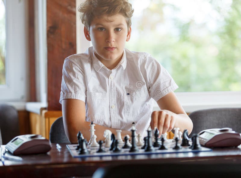 Śliczna 11 lat chłopiec w białej koszula, mądrze, siedzi w sali lekcyjnej szachowych na chessboard sztukach i Trenować, lekcja, h fotografia stock Śliczna 11 lat chłopiec w białej koszula, mądrze, siedzi w sali lekcyjnej szachowych na chessboard sztukach i Trenować, lekcja, h fotografia stock