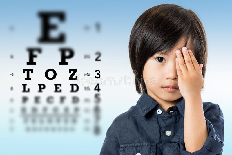 Close up portrait of handsome little asian boy testing eyesight.Kid closing one eye with hand against alphabetical out of focus eye test chart in background. Close up portrait of handsome little asian boy testing eyesight.Kid closing one eye with hand against alphabetical out of focus eye test chart in background.