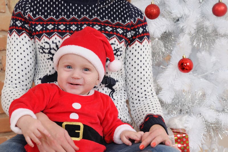Śliczna mała chłopiec w Santa kostiumu obsiadaniu na matek kolanach dalej obraz stock Śliczna mała chłopiec w Santa kostiumu obsiadaniu na matek kolanach dalej obraz stock