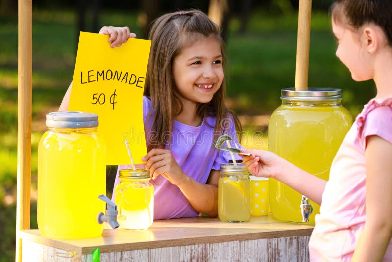 Cute little girl selling natural lemonade to kid in park. Summer refreshing drink. Cute little girl selling natural lemonade to kid in park. Summer refreshing drink