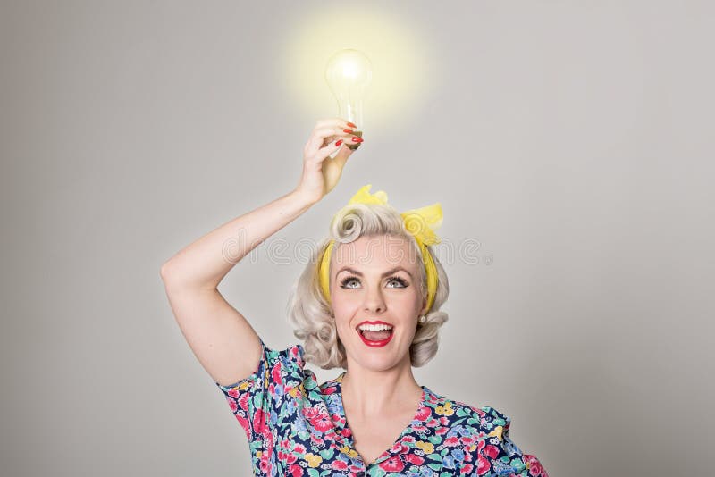 Ślicznej blondynki retro dziewczyna trzyma rozjarzoną żarówkę - humorystyczny przeciw fotografia stock Ślicznej blondynki retro dziewczyna trzyma rozjarzoną żarówkę - humorystyczny przeciw fotografia stock
