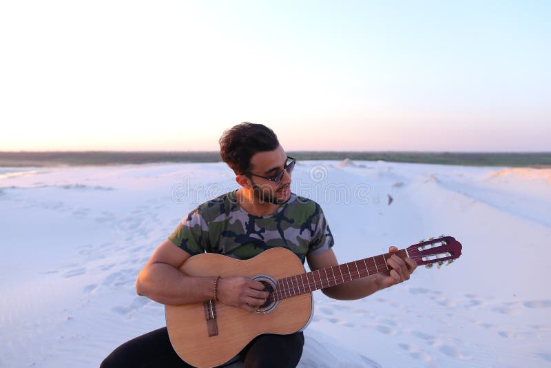 Śliczny młody męski arab cieszy się dźwięka gitara, siedzi na wzgórzu wewnątrz obrazy stock Śliczny młody męski arab cieszy się dźwięka gitara, siedzi na wzgórzu wewnątrz obrazy stock