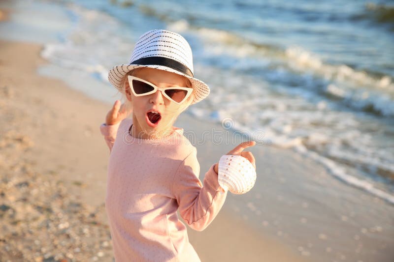 Śmieszna mała dziewczynka z denną skorupą na plaży zdjęcia stock Śmieszna mała dziewczynka z denną skorupą na plaży zdjęcia stock