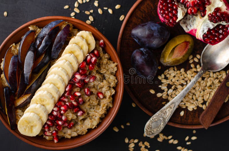 Śniadanie z miski z owsianką, bananem, nasionami granatu i śliwką na czarnym tle Widok z góry, płaski zdjęcie stock Śniadanie z miski z owsianką, bananem, nasionami granatu i śliwką na czarnym tle Widok z góry, płaski zdjęcie stock
