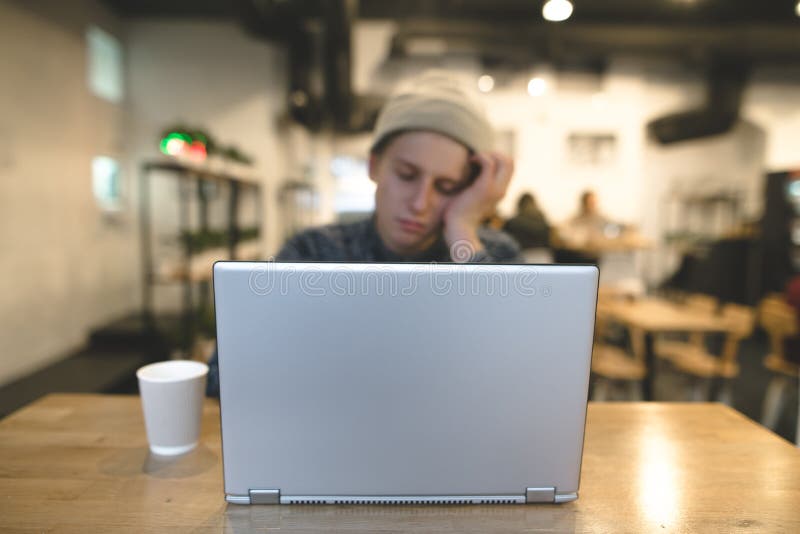 Śpiący freelancer siedzi w wygodnej kawiarni i pracuje dla laptopu Modnisie w kawiarni z laptopem Ostrość na laptopie zdjęcia stock Śpiący freelancer siedzi w wygodnej kawiarni i pracuje dla laptopu Modnisie w kawiarni z laptopem Ostrość na laptopie zdjęcia stock