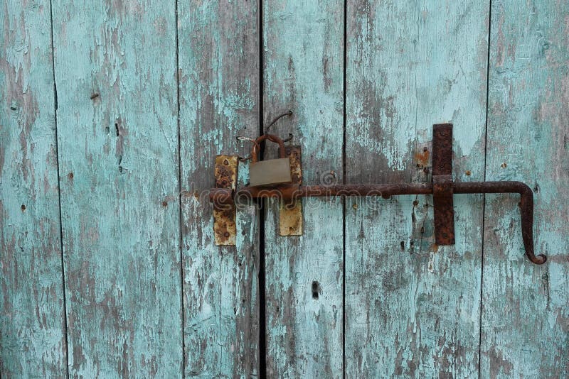 Rusty door bolt sliding latch and padlock on old weathered wooden gate with chipped blue paint. Rusty door bolt sliding latch and padlock on old weathered wooden gate with chipped blue paint