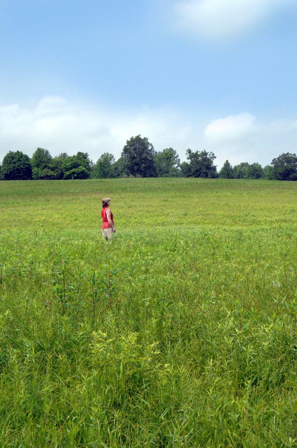 Woman stands in a large field feeling confused about life's choices. Woman is of mature age and facing retirement, financial and economy problems and field has no clear path or trail. Woman stands in a large field feeling confused about life's choices. Woman is of mature age and facing retirement, financial and economy problems and field has no clear path or trail.