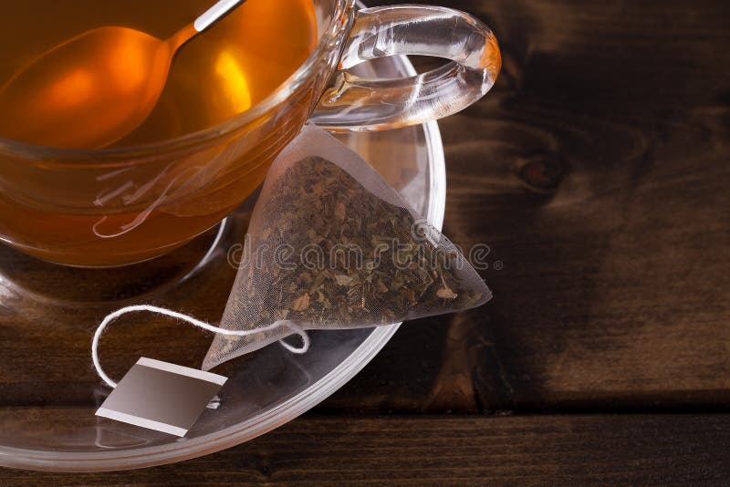 Fresh glass cup of tea with saucer and teabag close up. Set on a dark wooden table with space for text. Fresh glass cup of tea with saucer and teabag close up. Set on a dark wooden table with space for text