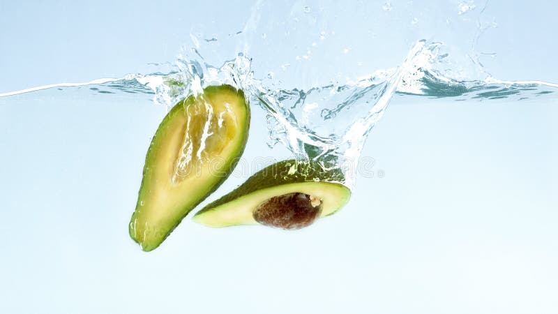 Świeże dojrzałe avocado połówki spada w wodzie fotografia stock Świeże dojrzałe avocado połówki spada w wodzie fotografia stock