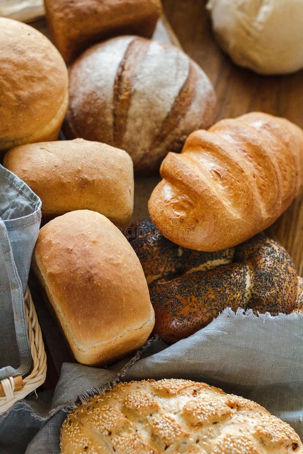 Freshly baked tasty white flour rhye and multi grain floor loafs of rectangular round and oval breads and plaited challah bread at wooden table grey linen kitchen towel at in bakery house. Freshly baked tasty white flour rhye and multi grain floor loafs of rectangular round and oval breads and plaited challah bread at wooden table grey linen kitchen towel at in bakery house