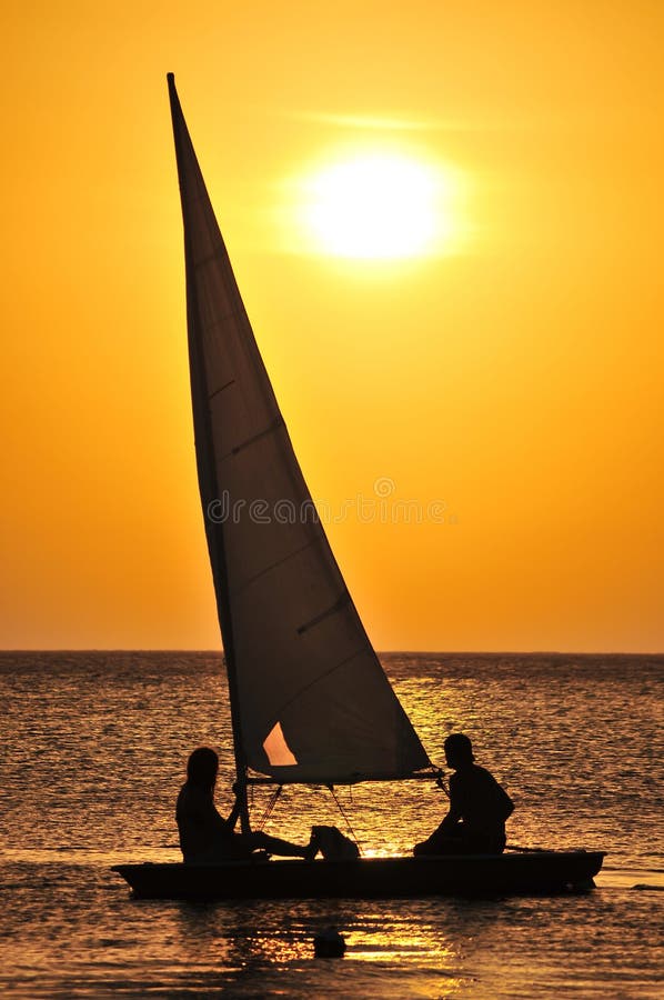 Two silhouetted people sailing yacht on sea with golden sunset background. Two silhouetted people sailing yacht on sea with golden sunset background.