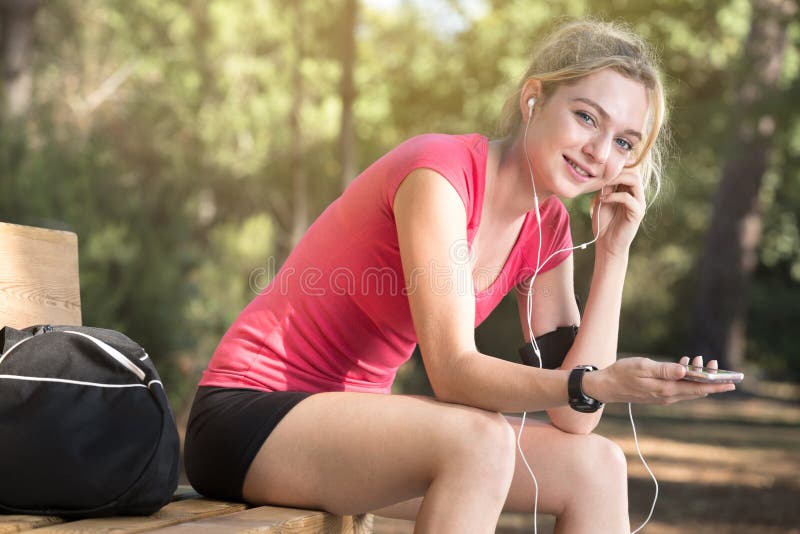 Żeńska atleta siedzi na ławce z hełmofonami zdjęcie royalty free Żeńska atleta siedzi na ławce z hełmofonami zdjęcie royalty free