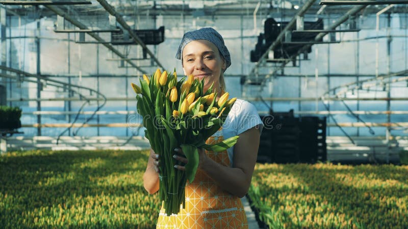 Żeńska ogrodniczka trzyma bukiet z tulipanami i uśmiechami przy kamerą
