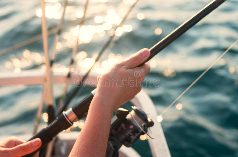 Female hand holding a fishing pole against the background of the sea. Sea fishing. The woman is fishing. Female hand holding a fishing pole against the background of the sea. Sea fishing. The woman is fishing