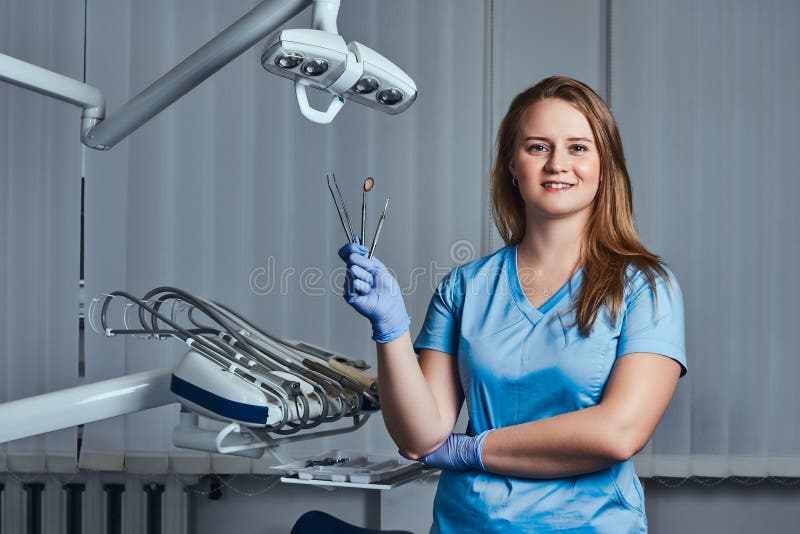 Żeński dentysta trzyma stomatologicznych narzędzia podczas gdy siedzący w jej dentysty biurze obrazy stock Żeński dentysta trzyma stomatologicznych narzędzia podczas gdy siedzący w jej dentysty biurze obrazy stock