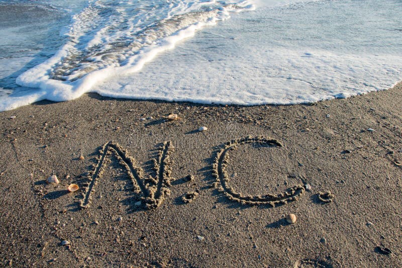 The letters N and C written in the sand on a North Carolina Beach as waves and water roll in. The letters N and C written in the sand on a North Carolina Beach as waves and water roll in