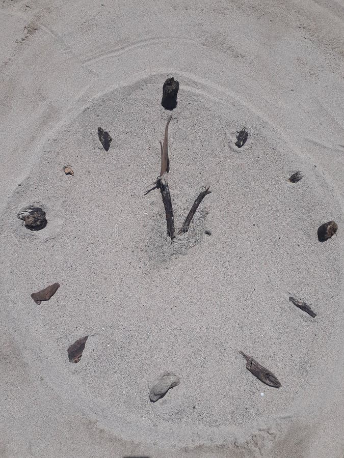 A clock face made on the beach in sand with sticks for hands and stones for hours. A clock face made on the beach in sand with sticks for hands and stones for hours