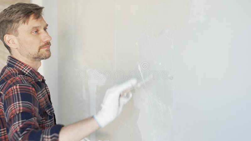 Άνδρας οικοδόμος που απλώνει γύψο σε λευκό τοίχο φορώντας προστατευτικά γάντια κατά τη διάρκεια του σπιτιού απόθεμα βίντεο
