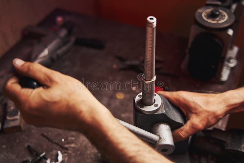 Male straightening the form of ring on mandrel with measuring scale while turning the lever of device. Male straightening the form of ring on mandrel with measuring scale while turning the lever of device