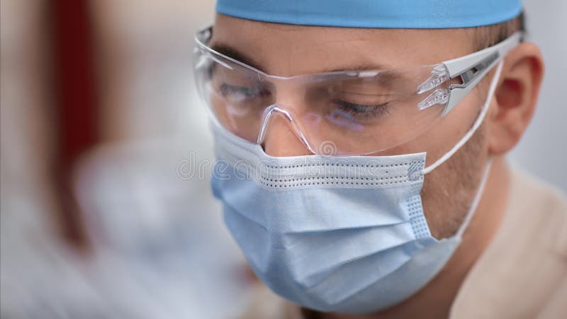 άνδρας στοματολόγος με αυτοπεποίθηση που κλείνει το πρόσωπο με προστατευτική ιατρική μάσκα φιλμ μικρού μήκους