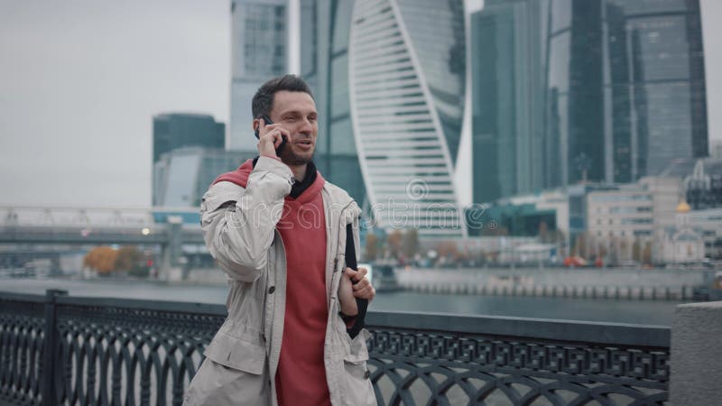 άνδρας χαμογελά περπατώντας με τηλέφωνο στο φόντο των επιχειρηματικών ουρανοξύστων