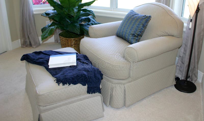 Comfortable and relaxing corner of bedroom, showing oversized lounging chair with matching ottoman and carpet and blue pillow and throw. Easy chair. Comfortable and relaxing corner of bedroom, showing oversized lounging chair with matching ottoman and carpet and blue pillow and throw. Easy chair.