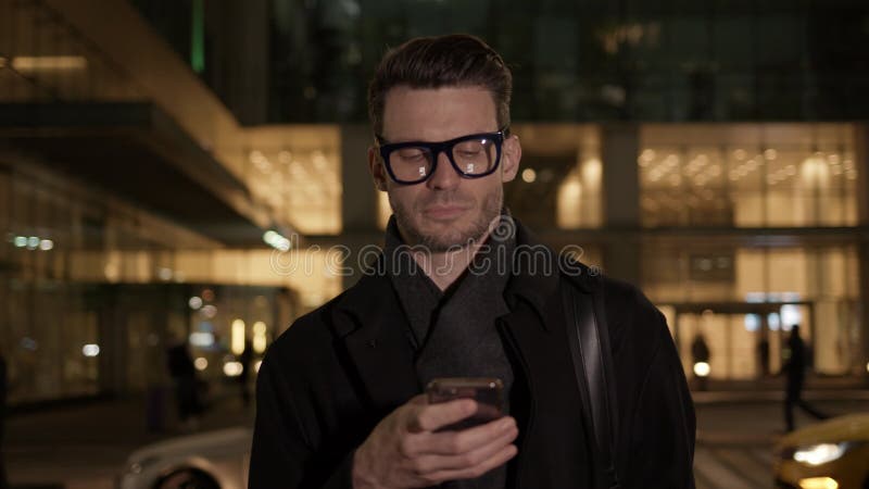 άντρας με γυαλιά με τηλέφωνο στο παρασκήνιο του εργοταξίου τη νύχτα