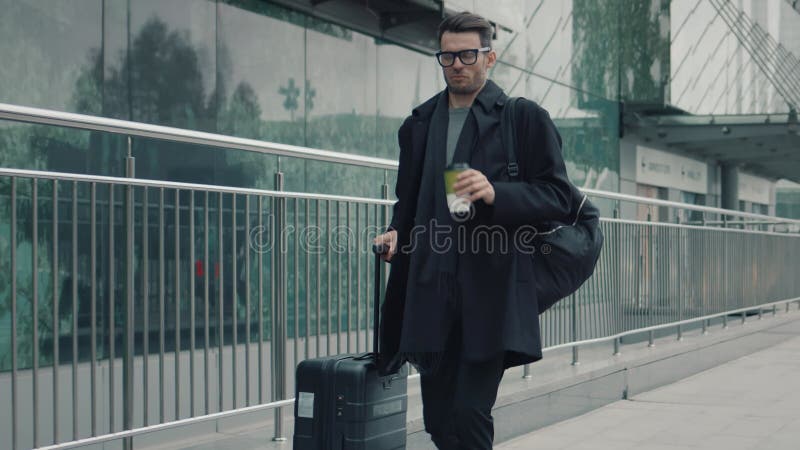 άντρας με μαύρο παλτό με βαλίτσα στο φόντο του τερματικού του αεροδρομίου
