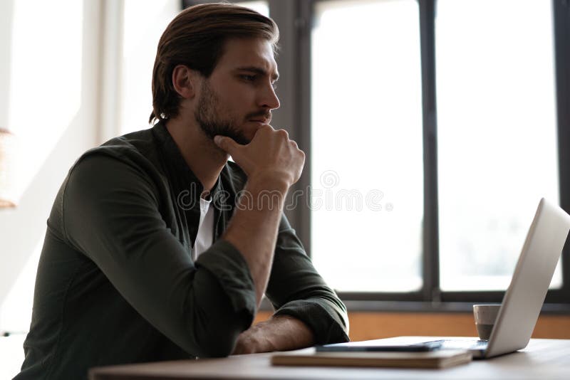 άντρας με μολύβι που κάθεται στο τραπέζι και εργάζεται σε φορητό υπολογιστή σκεπτόμενος την προβληματική λύση στοκ εικόνες