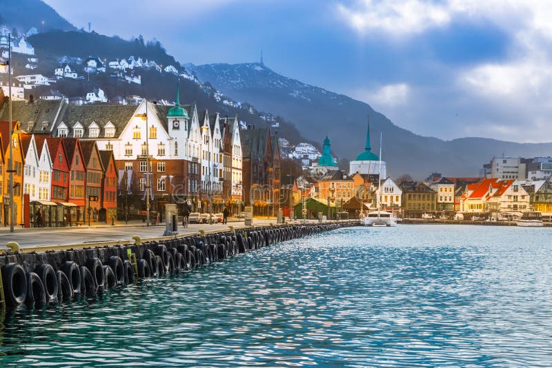 Historical wooden houses at the port of Bergen in Norway. Popular street to the city center along the waterfront. Mountain in the background. Famous travel destination in Scandinavia. Cityscape and skyline with lights at twilight. Historical wooden houses at the port of Bergen in Norway. Popular street to the city center along the waterfront. Mountain in the background. Famous travel destination in Scandinavia. Cityscape and skyline with lights at twilight.