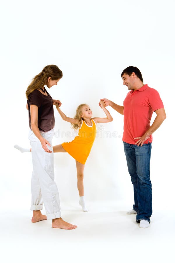 Image of young girl doing exercise holding her parents by hands. Image of young girl doing exercise holding her parents by hands