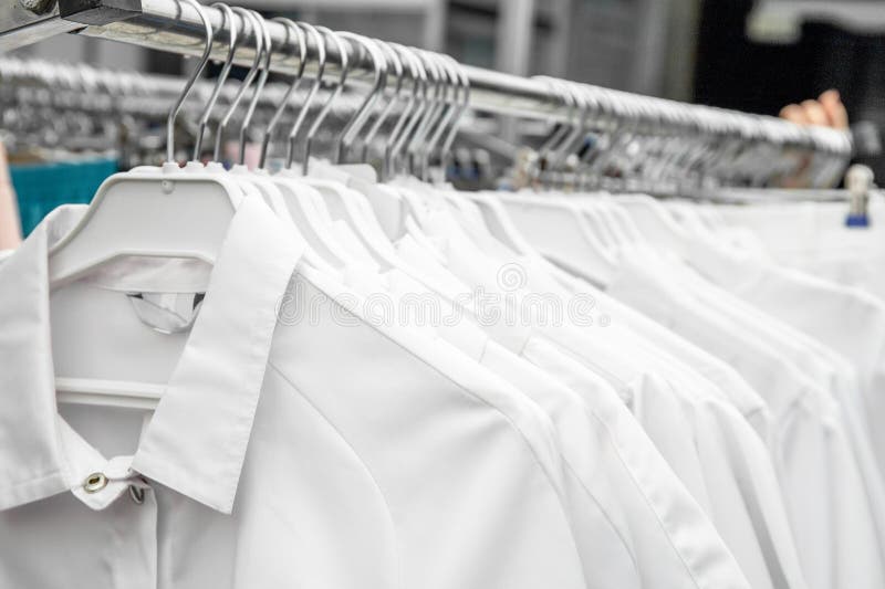 Άσπρα ιατρικά ομοιόμορφα ενδύματα στις κρεμάστρες στο κατάστημα ή στο νοσοκομείο στοκ εικόνες Άσπρα ιατρικά ομοιόμορφα ενδύματα στις κρεμάστρες στο κατάστημα ή στο νοσοκομείο στοκ εικόνες