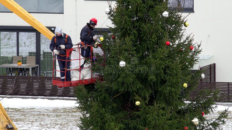 Άτομα Laborer στο γερανό που κρεμά τις ζωηρόχρωμες σφαίρες στο χριστουγεννιάτικο δέντρο στην αστική περιοχή