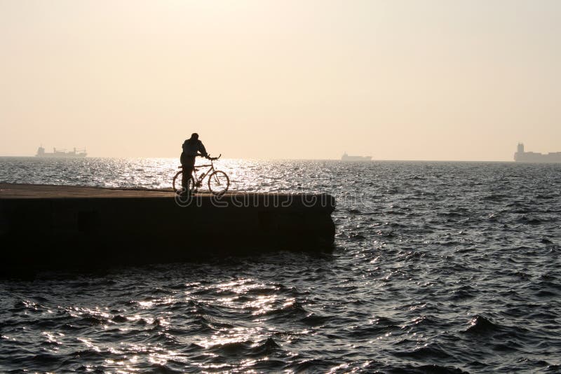 A man's sillouette with a bicycle by the sea at sunset. A man's sillouette with a bicycle by the sea at sunset