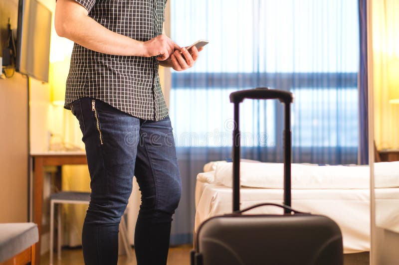 Man using smartphone in hotel room with baggage and suitcase. Tourist with mobile phone in holiday rental apartment. Calling taxi cab or doing online check-in. Travel and smart technology concept. Man using smartphone in hotel room with baggage and suitcase. Tourist with mobile phone in holiday rental apartment. Calling taxi cab or doing online check-in. Travel and smart technology concept.