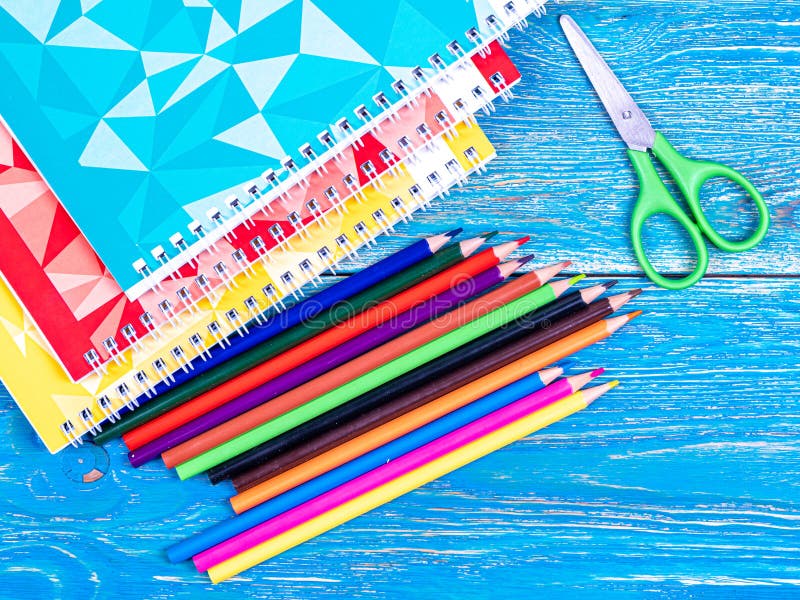 Colored pencils and notebooks with colored covers on a wooden table. September 1. Design. Background. High quality photo. Colored pencils and notebooks with colored covers on a wooden table. September 1. Design. Background. High quality photo