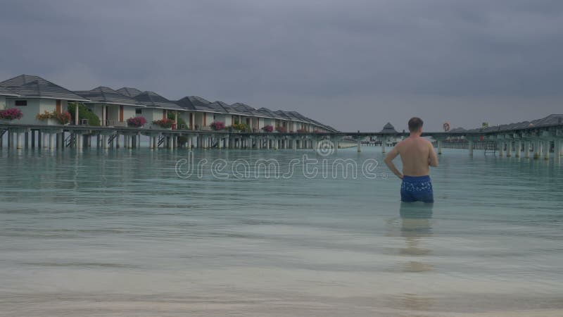 Ένα άτομο μπαίνει σε τον ωκεανό, που στέκεται μπροστά από τις βίλες νερού Άσπρη αμμώδης παραλία των Μαλδίβες
