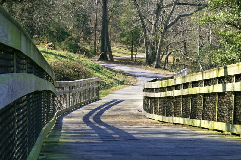 A winding green way trail that crosses over a bridge and then travels off to a distant destination. The trail follows the Neuse river in North Carolina. A winding green way trail that crosses over a bridge and then travels off to a distant destination. The trail follows the Neuse river in North Carolina.