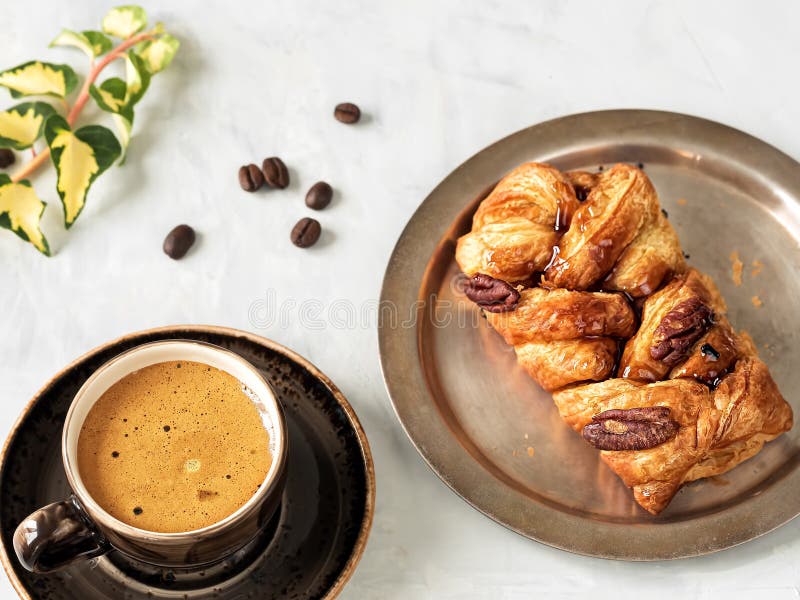 A brown cup with espresso next to maple pecans with nuts and syrup. Fresh coffee beans, ivy branch. Located on a gray background. Top view. A brown cup with espresso next to maple pecans with nuts and syrup. Fresh coffee beans, ivy branch. Located on a gray background. Top view.