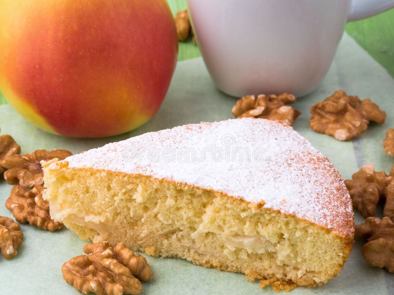 A piece of Charlotte on parchment, nuts, apple and cup of tea. Apple pie decorated with icing sugar. A piece of Charlotte on parchment, nuts, apple and cup of tea. Apple pie decorated with icing sugar