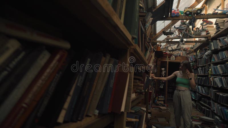 ένα κορίτσι με μια όμορφη φιγούρα χαμογελά και παίρνει ένα βιβλίο σε ένα ράφι στη βιβλιοθήκη