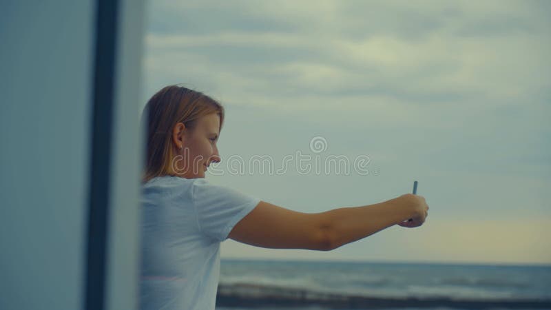 ένα κορίτσι παίρνει μια σέλφι στο φόντο της θάλασσας όπου ξεκινά ο άνεμος και η καταιγίδα.